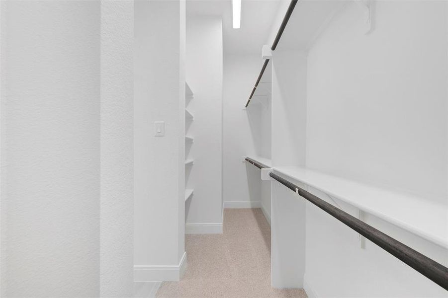 Expansive walk-in closet featuring built-in shelving, two levels of hanging rods, and neutral carpeting Expansive walk-in closet featuring built-in shelving, two levels of hanging rods, and neutral carpeting
