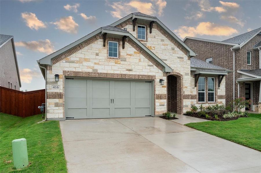 French country inspired facade with stone siding, driveway, and a garage