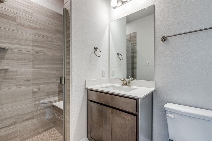 Full bath featuring toilet, vanity, a stall shower, and a textured wall
