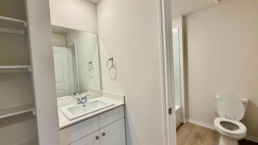 Bathroom featuring a white vanity with an integrated sink, a rectangular wall-mounted mirror, and wood-finish flooring