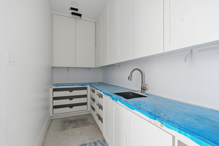 This walk in pantry doubles as a prep kitchen, featuring custom built cabinetry, dedicated drawer storage, and a secondary prep sink. Final finishes include checkered tile flooring for a polished, functional workspace.