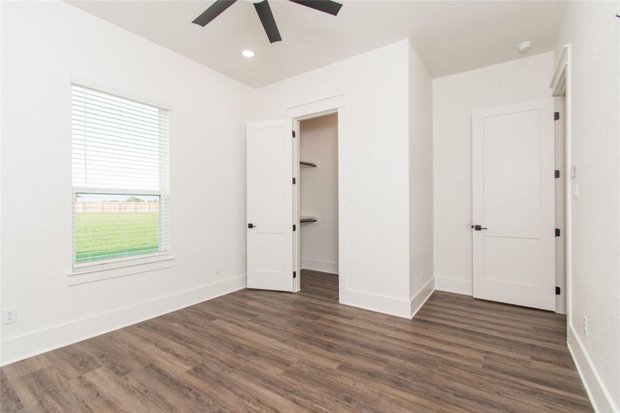 A well-lit bedroom features durable plank flooring and convenient built-in closet shelving.