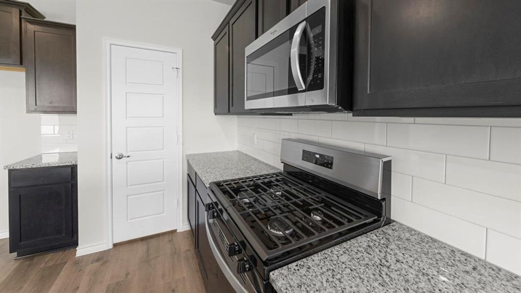 Gourmet kitchen featuring dark wood cabinetry, stainless steel range with gas burners, stainless steel over-the-range microwave, granite countertops, and white subway tile backsplash Gourmet kitchen featuring dark wood cabinetry, stainless steel range with gas burners, stainless steel over-the-range microwave, granite countertops, and white subway tile backsplash