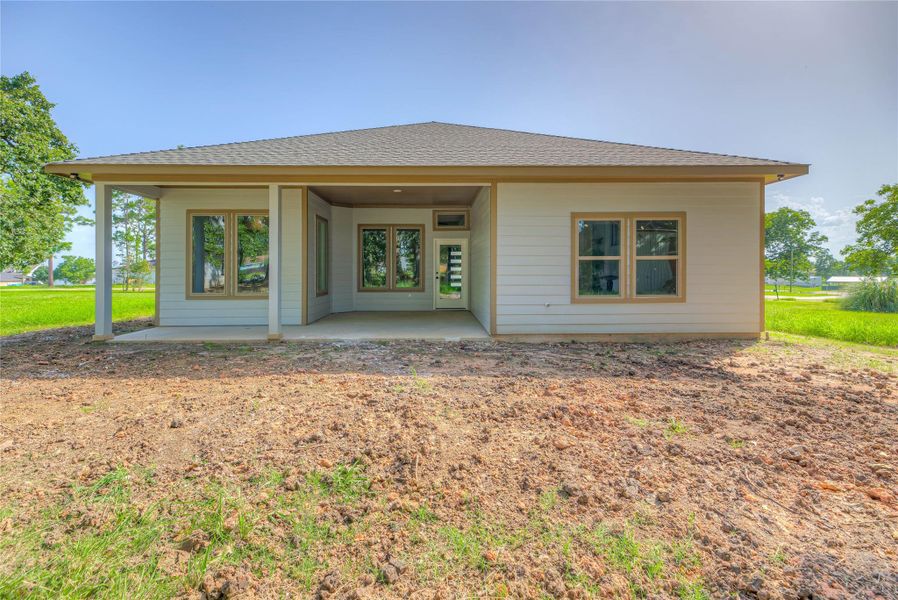 The back of the home with a covered patio. The house features large windows and a simple, clean design, set in a spacious, backyard.