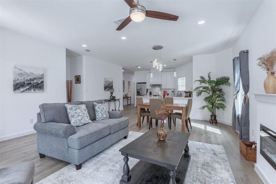 Living room with ceiling fan with notable chandelier and light hardwood / wood-style flooring