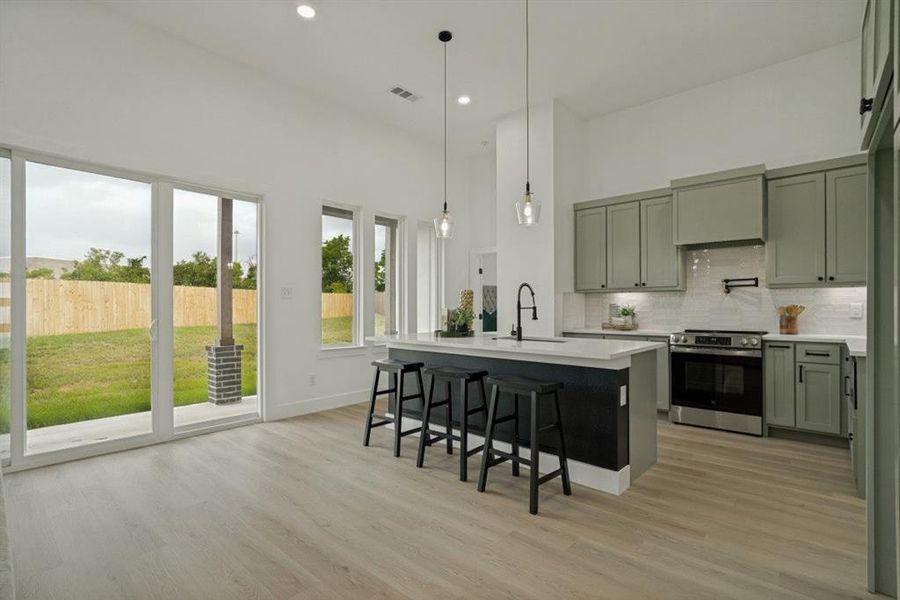 Modern kitchen featuring light green cabinetry, stainless steel appliances, and a central island with integrated sink Modern kitchen featuring light green cabinetry, stainless steel appliances, and a central island with integrated sink