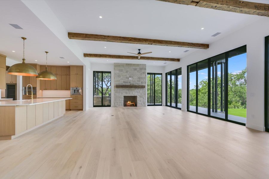 A spacious great room showcases warm wood beams, a stone fireplace, and abundant natural light from numerous glass doors.