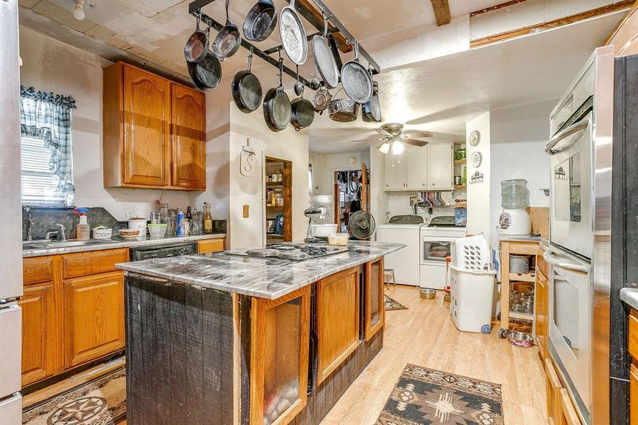 Kitchen featuring brown cabinetry, washer and dryer, light wood-style flooring, a center island, and stainless steel double oven Kitchen featuring brown cabinetry, washer and dryer, light wood-style flooring, a center island, and stainless steel double oven