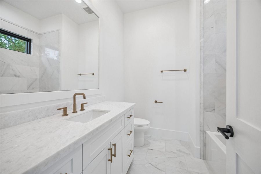 Marble tile climbs the wall while a wide window provides natural light and privacy. Brass fixtures warm the clean palette. *Previous Project*