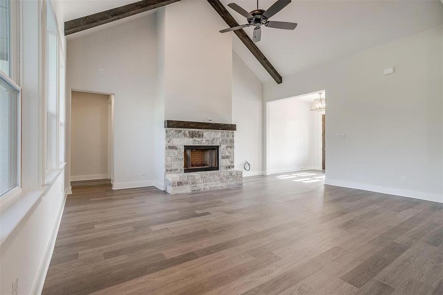 Unfurnished living room with ceiling fan, high vaulted ceiling, a stone fireplace, and wood-type flooring