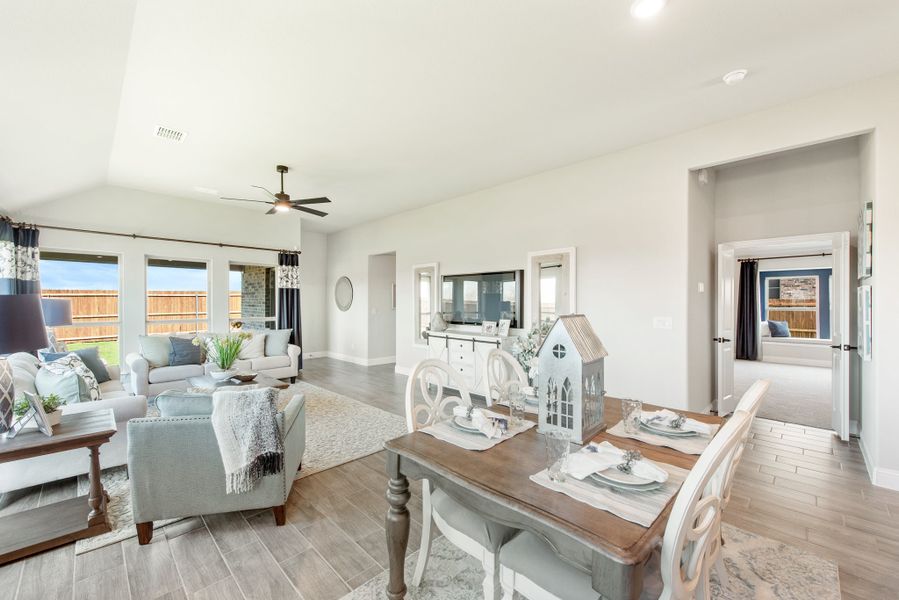Open-concept living and dining area with vaulted ceiling, ceiling fan, wood-look floors, and large windows