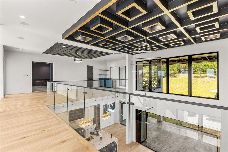 Hardwood flooring across an open-concept upper level, featuring glass railings and a coffered ceiling with integrated lighting