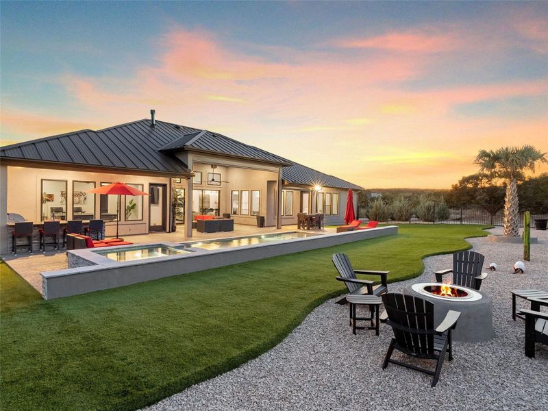 Back of property at dusk with a yard, a patio, an outdoor living space with a fire pit, a pool with connected hot tub, and a standing seam roof