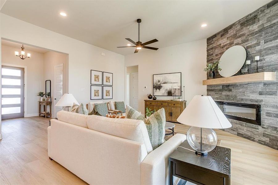 Living room with light hardwood / wood-style floors, ceiling fan with notable chandelier, and a stone fireplace