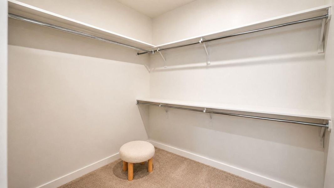 Walk-in closet featuring carpeted flooring and multiple tiers of built-in shelving with metal hanging rods. A small upholstered stool sits in the corner.