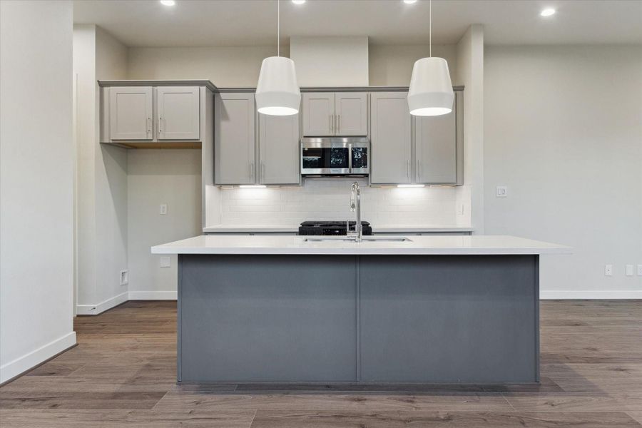 A modern kitchen centers around a large quartz island with pendant lighting, perfect for gathering, meal prep, and casual dining.