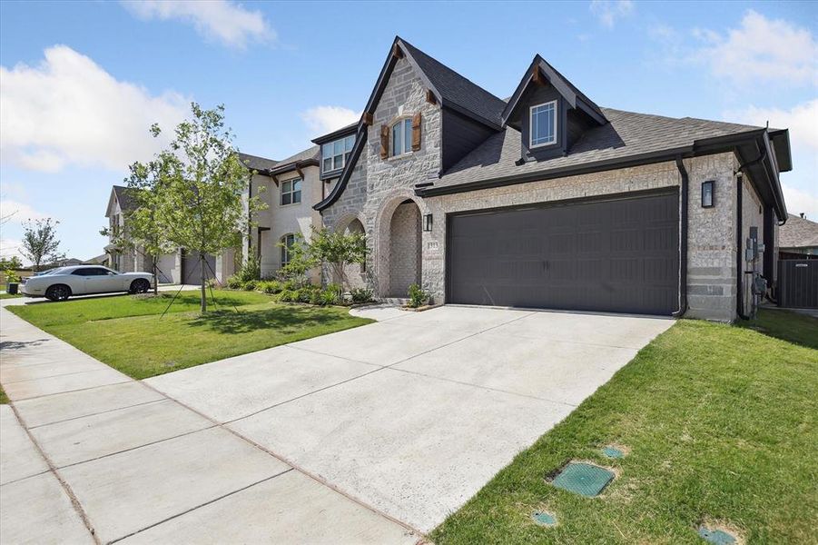 French country inspired facade with stone siding, driveway, a front yard, an attached garage, and central air condition unit