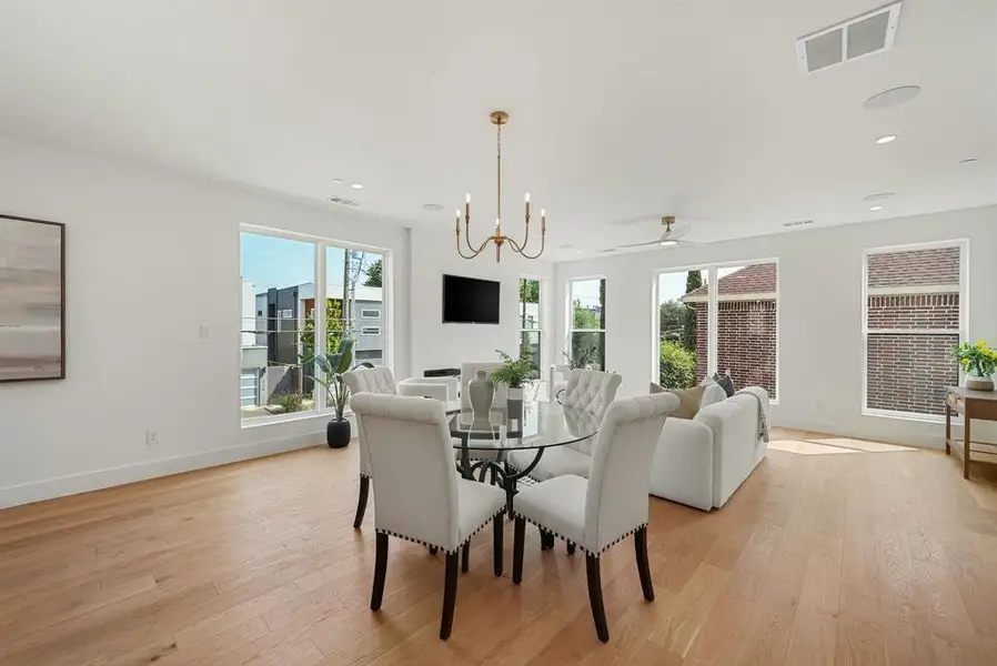 Open-concept living space with light wood-finish flooring, numerous windows, and a modern chandelier Open-concept living space with light wood-finish flooring, numerous windows, and a modern chandelier