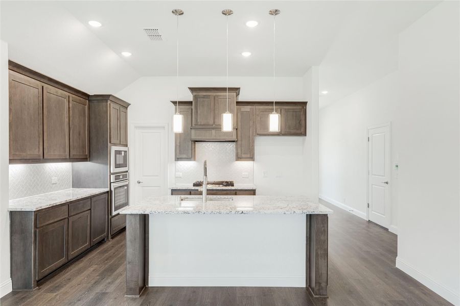 Kitchen with dark wood cabinets, granite island, pendant lights, and herringbone tile backsplash on hardwood floors. Kitchen with dark wood cabinets, granite island, pendant lights, and herringbone tile backsplash on hardwood floors.