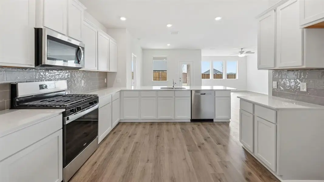 Modern kitchen featuring white cabinetry, stainless steel appliances, light countertops, and wood-finish flooring Modern kitchen featuring white cabinetry, stainless steel appliances, light countertops, and wood-finish flooring