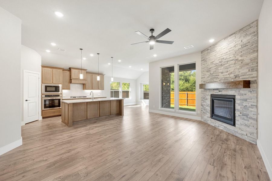 Open-concept living area with stone fireplace, wood floors, and kitchen with island and wood cabinets