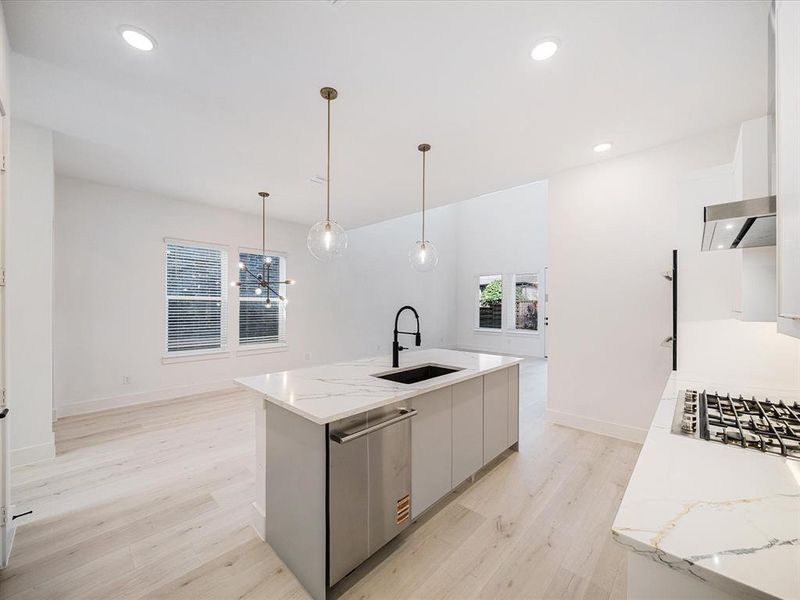 Kitchen featuring an island with sink, light wood finished floors, light stone countertops, pendant lighting, and recessed lighting