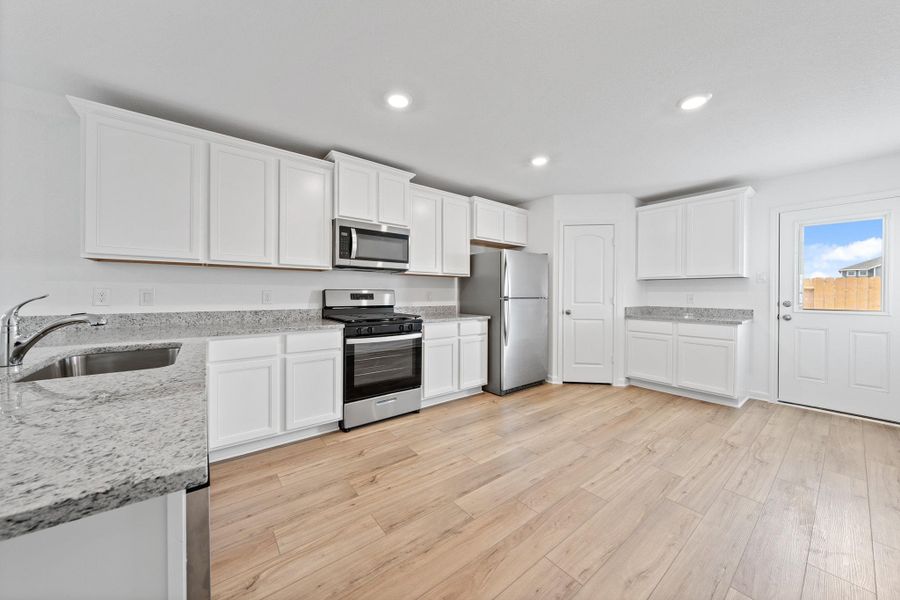 Kitchen featuring stainless steel appliances, white cabinets, light stone countertops, light wood-style floors, and recessed lighting