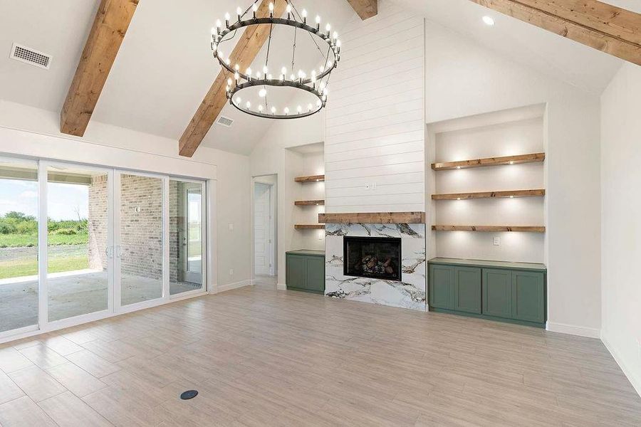 Unfurnished living room featuring beamed ceiling, high vaulted ceiling, light wood finished floors, a fireplace, and a chandelier