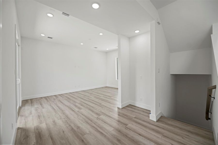 The living area showcases a bright and spacious room with modern LVP flooring, recessed lighting, and neutral walls. It features an open layout with a staircase leading down, ideal for versatile use and customization.