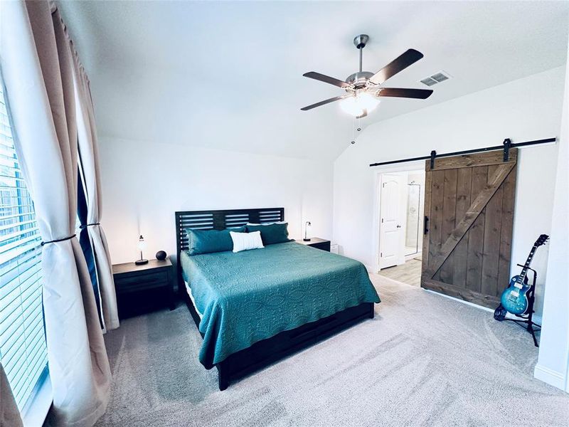 Carpeted bedroom with a barn door, lofted ceiling, and ceiling fan