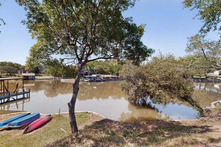 Waterfront property featuring a private boat dock, mature trees, and a spacious grassy area along the water's edge