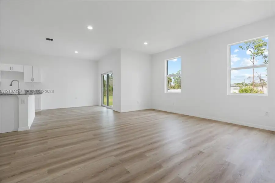 Open-concept interior featuring wood-finish flooring, recessed lighting, expansive windows, glass sliding door, and kitchen peninsula with stone-surface countertop Open-concept interior featuring wood-finish flooring, recessed lighting, expansive windows, glass sliding door, and kitchen peninsula with stone-surface countertop