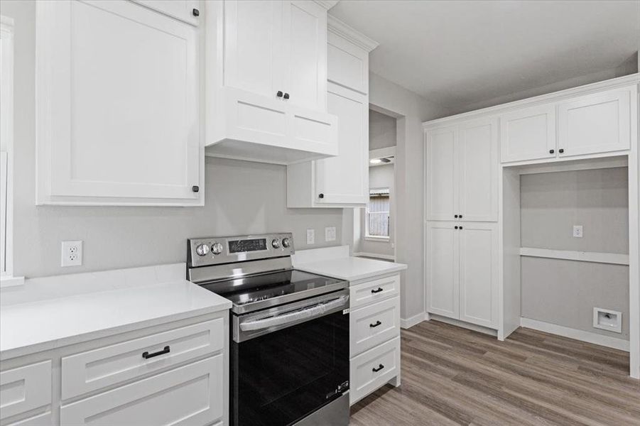 Kitchen with electric range, white cabinetry, and light hardwood / wood-style flooring