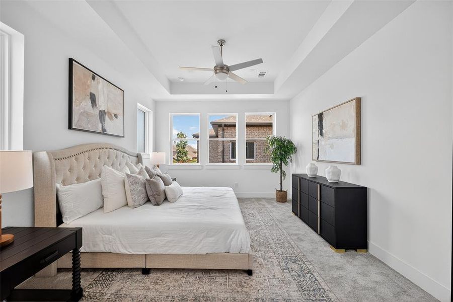 Bedroom featuring light carpet, a tray ceiling, and ceiling fan