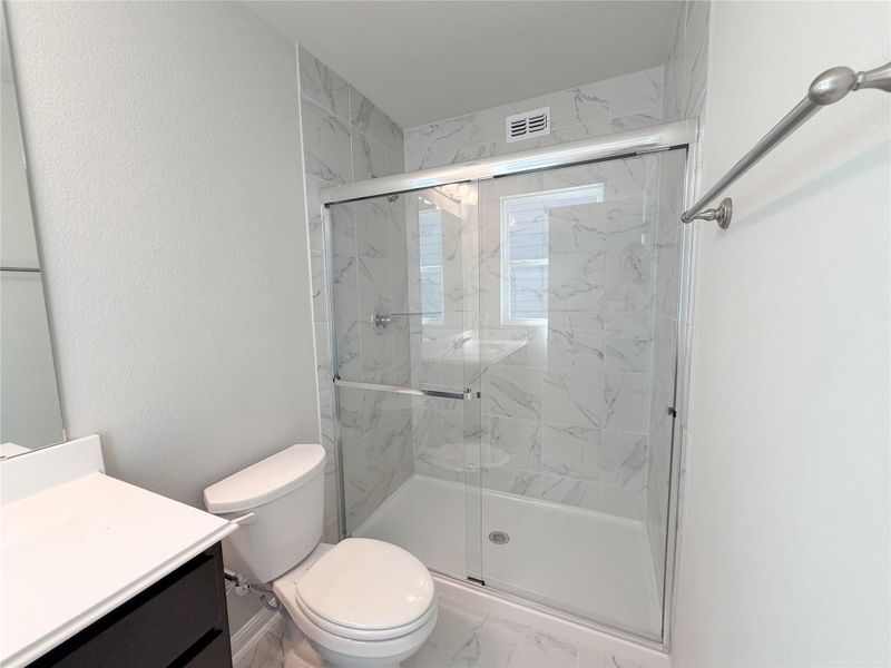 Shower with sliding glass doors, white tiled walls with marble-look veining, and a white shower pan