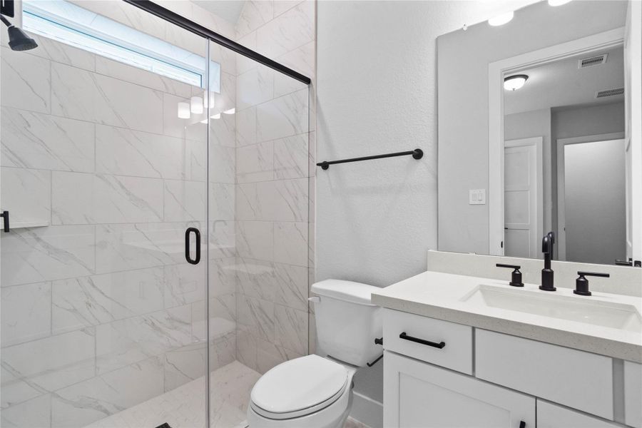 The private en suite bathroom features a modern vanity with light countertop, and a walk-in shower with sleek tile surround.