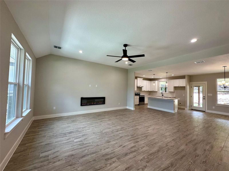 Unfurnished living room with wood finished floors, a ceiling fan, a glass covered fireplace, recessed lighting, and a chandelier Unfurnished living room with wood finished floors, a ceiling fan, a glass covered fireplace, recessed lighting, and a chandelier
