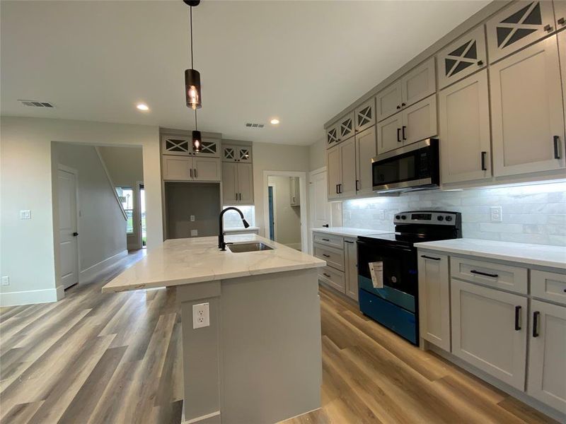 Kitchen with backsplash, light hardwood / wood-style flooring, stainless steel appliances, sink, and a center island with sink