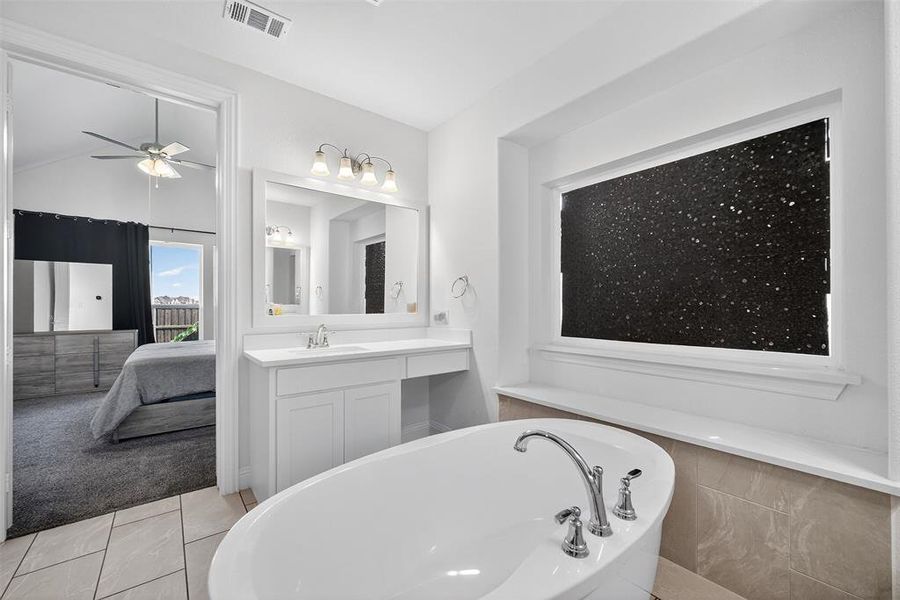 Full bath featuring a freestanding tub, vanity, ensuite bath, light tile patterned floors, and a ceiling fan Full bath featuring a freestanding tub, vanity, ensuite bath, light tile patterned floors, and a ceiling fan