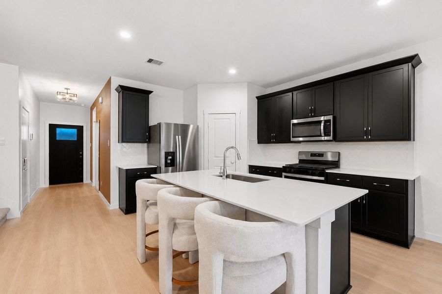 The kitchen showcases a generous island with seating, paired with elegant dark cabinetry, stainless steel appliances, and a refined, modern backsplash.