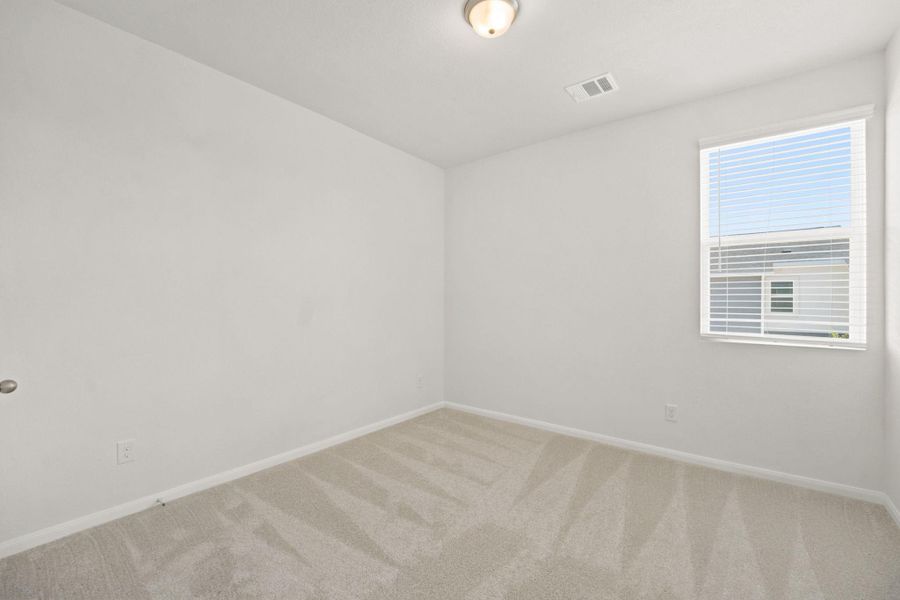 Plush carpeting and a large window define this versatile secondary bedroom space.