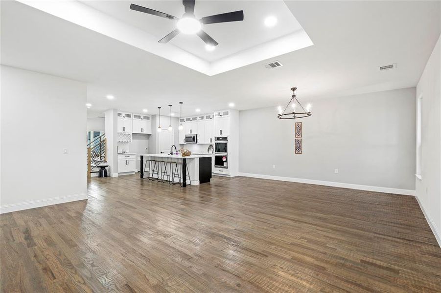 Living room featuring recessed lighting, a raised ceiling, a ceiling fan, a chandelier, and dark wood-style floors