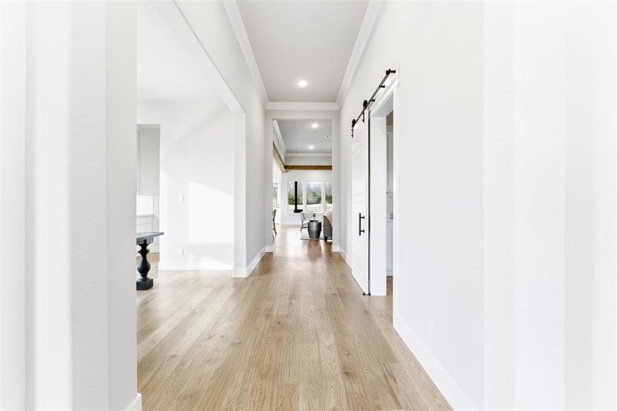 Hall featuring a barn door, crown molding, light wood finished floors, and recessed lighting