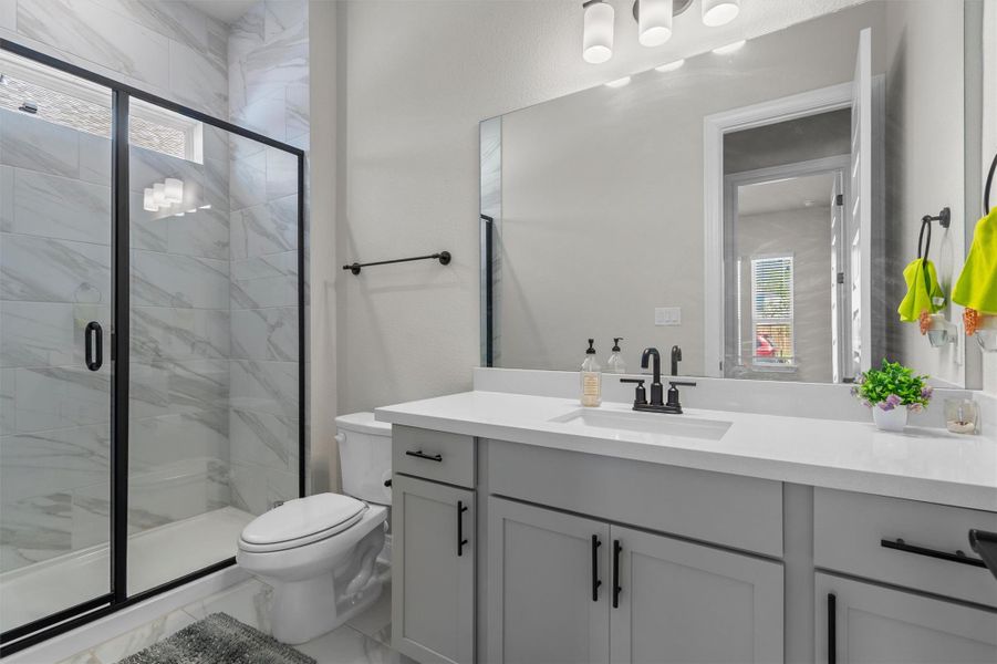 Polished tile surrounds a glass-enclosed shower alongside a modern stone-counter vanity.
