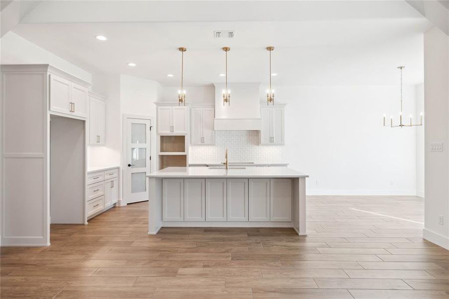 Kitchen featuring a kitchen island with sink, white cabinets, and pendant lighting