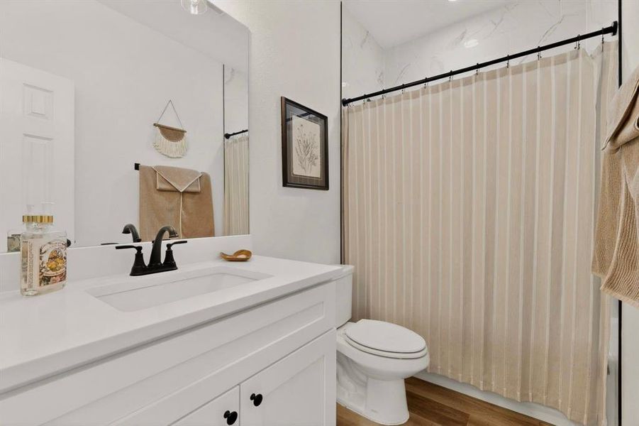 Bathroom featuring a white vanity with integrated sink, black fixtures, and a shower with white tile surround