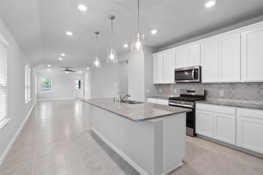 As you step past the entryway, you are immediately welcomed by a bright, open-concept kitchen that serves as the home's focal point. The space feels clean and modern, anchored by a large granite-topped island that seamlessly connects the cooking area to a long, light-filled living space.