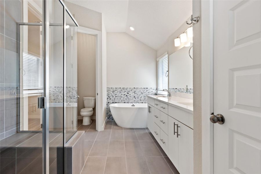 Bathroom with double vanity, tile walls, light tile patterned flooring, a shower stall, and a freestanding tub