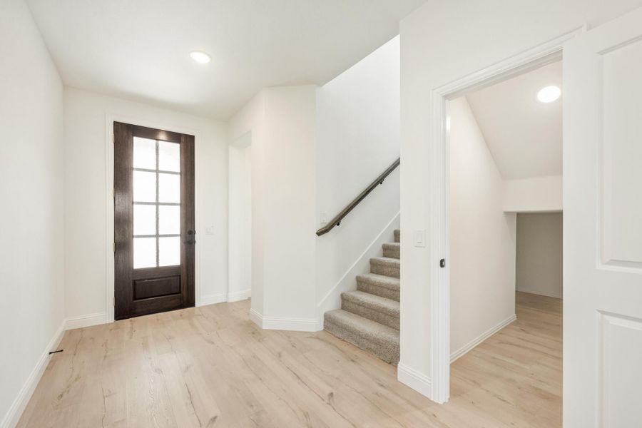Entryway with dark wood front door, light hardwood floors, and carpeted staircase leading to upper level