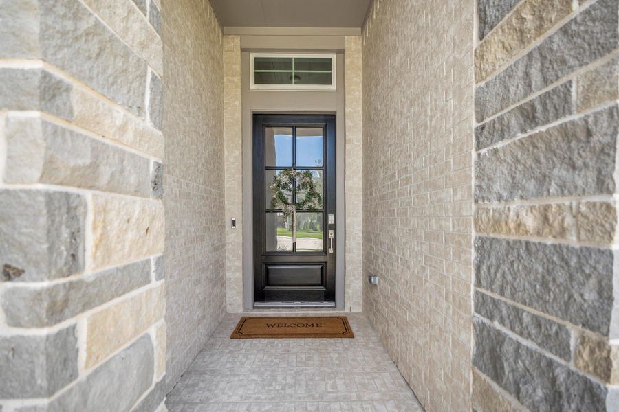 A tall, sheltered entry framed in brick creates a warm welcome, while the glass-paneled front door and overhead transom invite natural light inside.